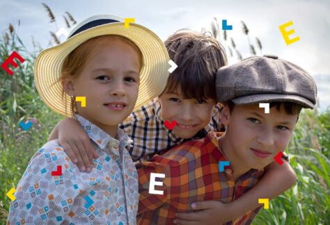 Dwóch chłopców i dziewczynka uśmiechają się do obiektywu. Dookoła trawa.