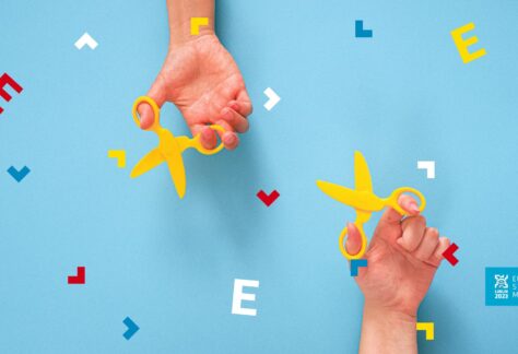 Na niebieskim tle dłonie dwóch osób, które trzymają żółte nożyczki.