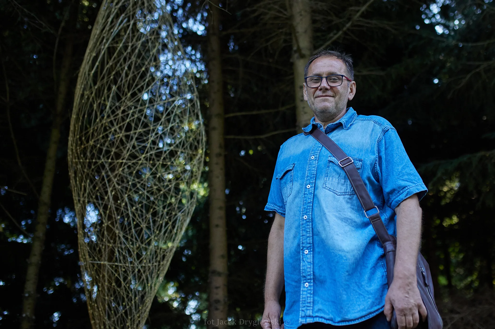 Mężczyzna stoi przy wyplecionej przez siebie pajęczynie z wikliny.