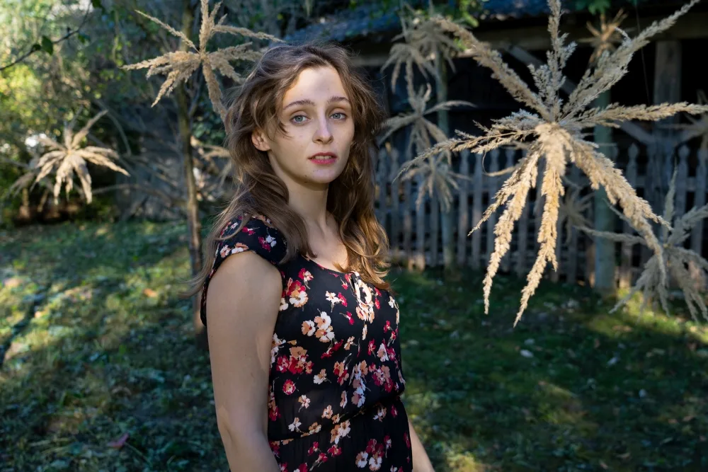 Dziewczyna stoi otoczona drzewami, na których są zawieszone kwiaty zrobione przez warsztatowiczkę.