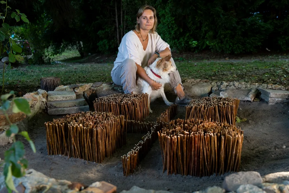 Kobieta z psem siedzą przy instalacji artystycznej z wikliny w kształcie krzyża.