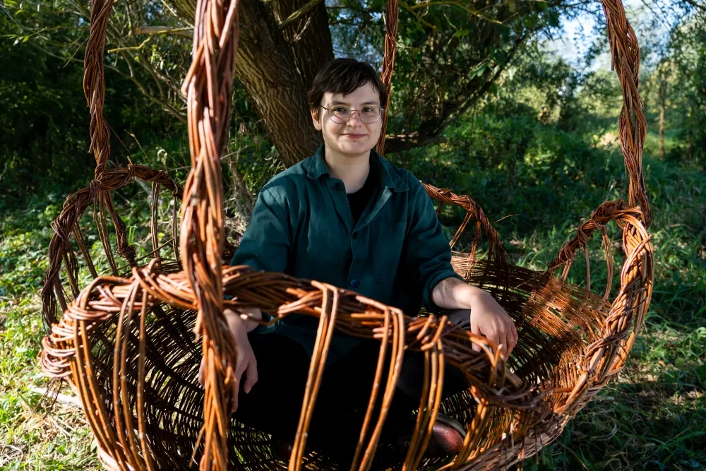 Dziewczyna siedzi w wiklinowym koszyku, który sama uplotła.