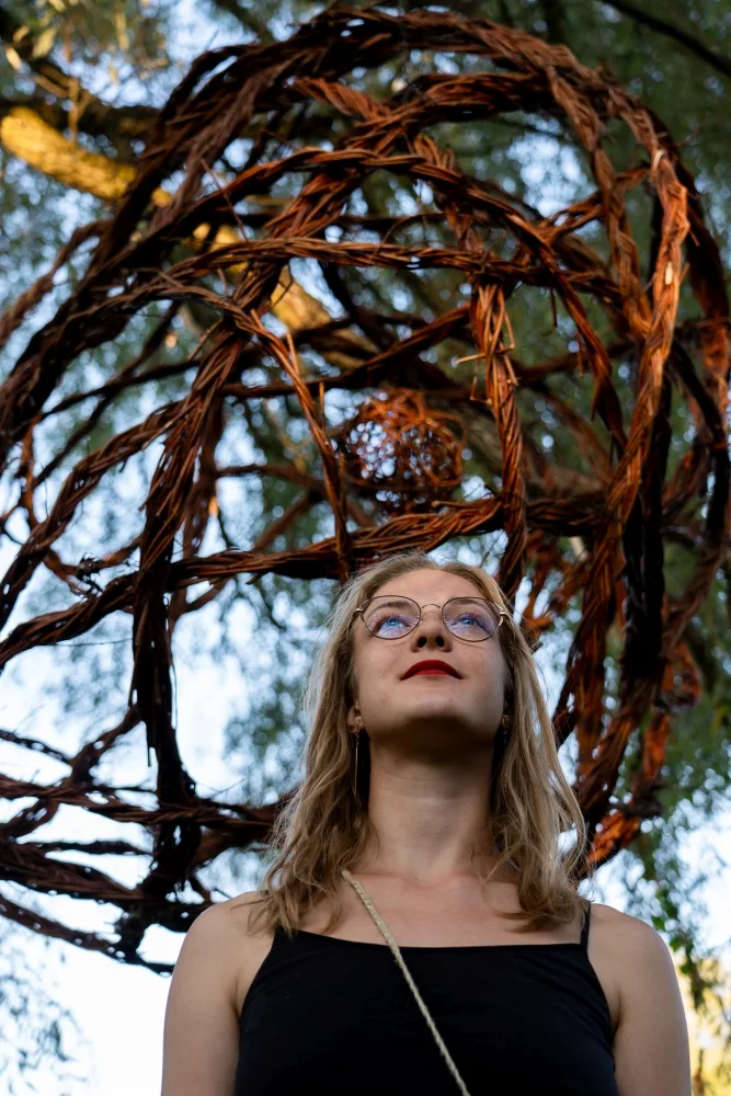 Kobieta stoi pod pajęczyną zawieszoną na drzewie.