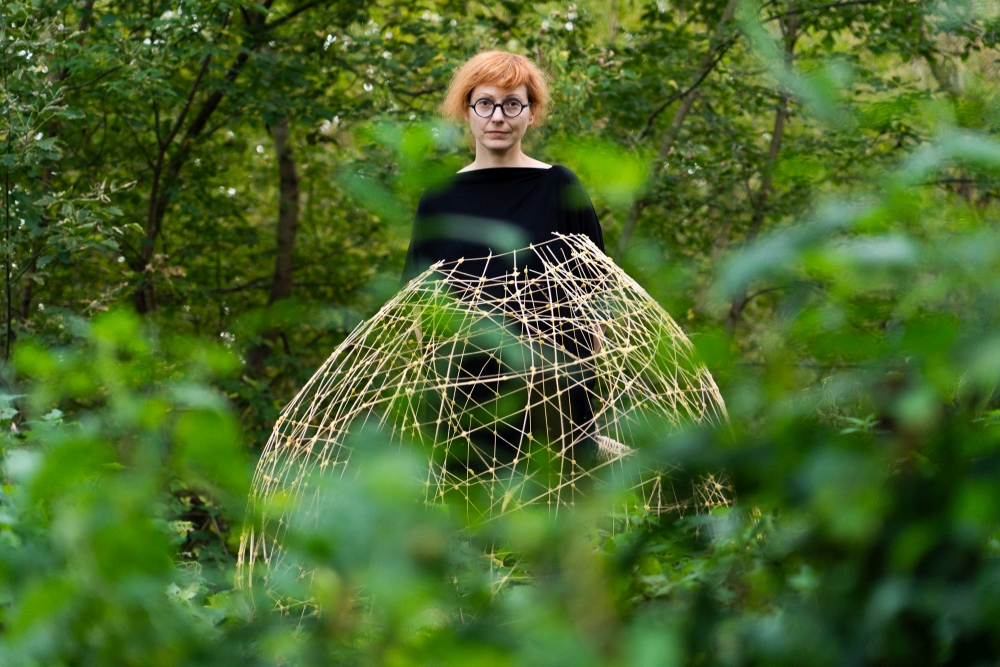 Kobieta stoi w lesie i prezentuje swoją pracę. To ażurowe koło.
