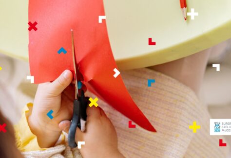 Dłonie dziecka przecinają nożyczkami kawałek papieru.