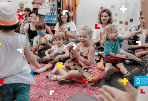 Dzieci z rodzicami siedzą na różowym dywanie i grają na ukulele.