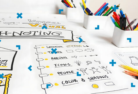 Na stole leżą notatki wizualne oraz stoją pudełka z flamastrami.