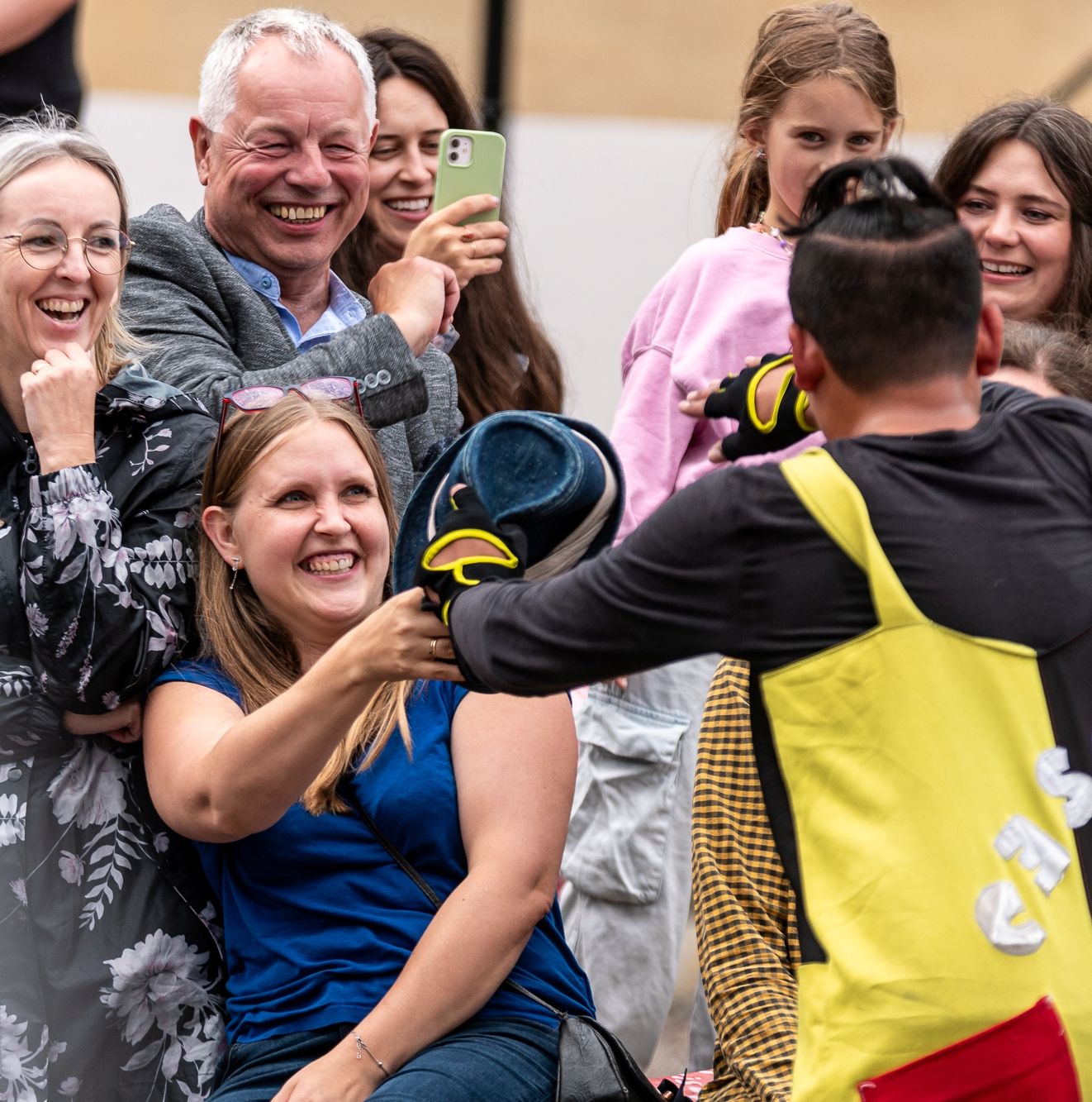 Plecy sztukmistrza ulicznego, który podaje swój kapelusz dziewczynie z publiczności.