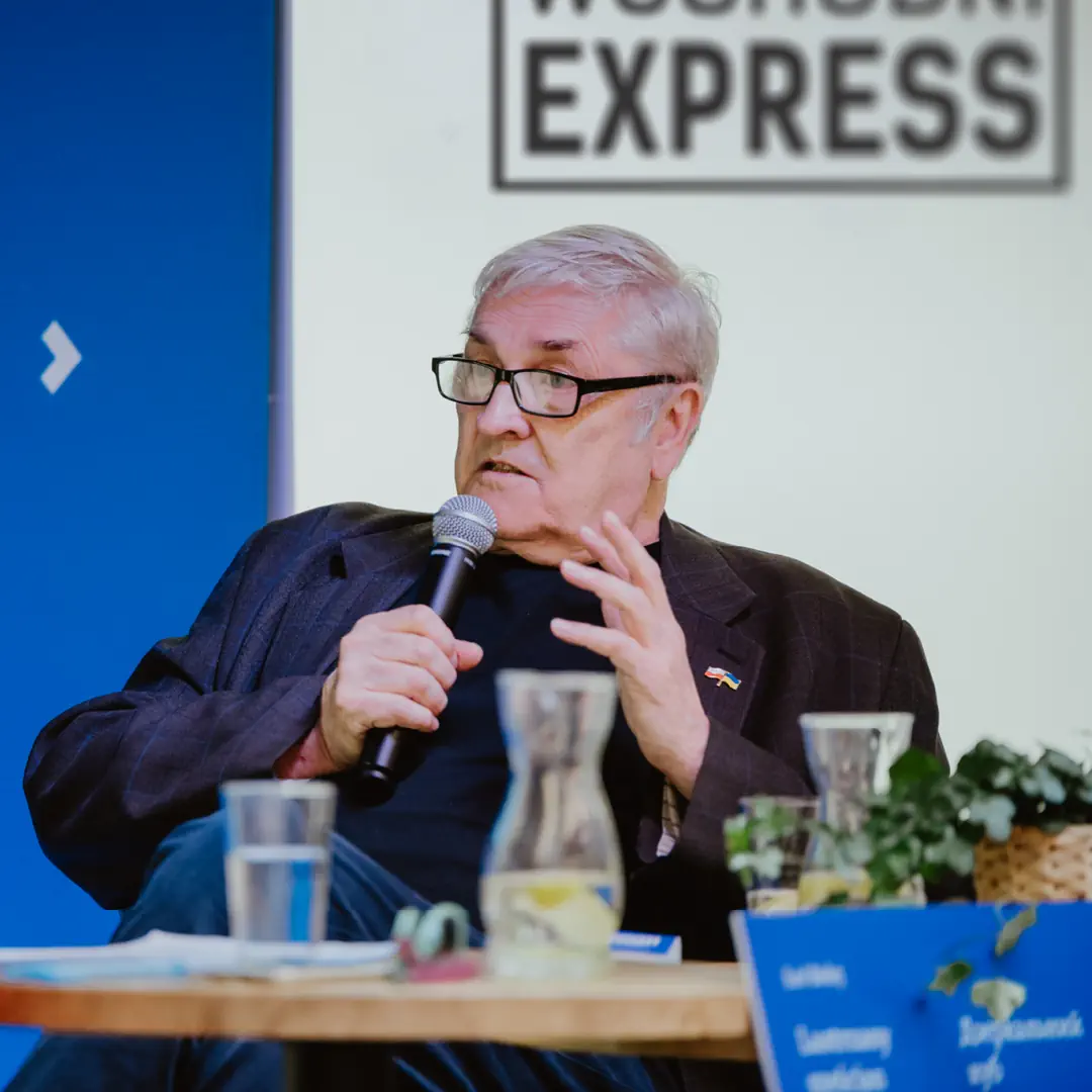 Starszy mężczyzna przemawia przez mikrofon.
