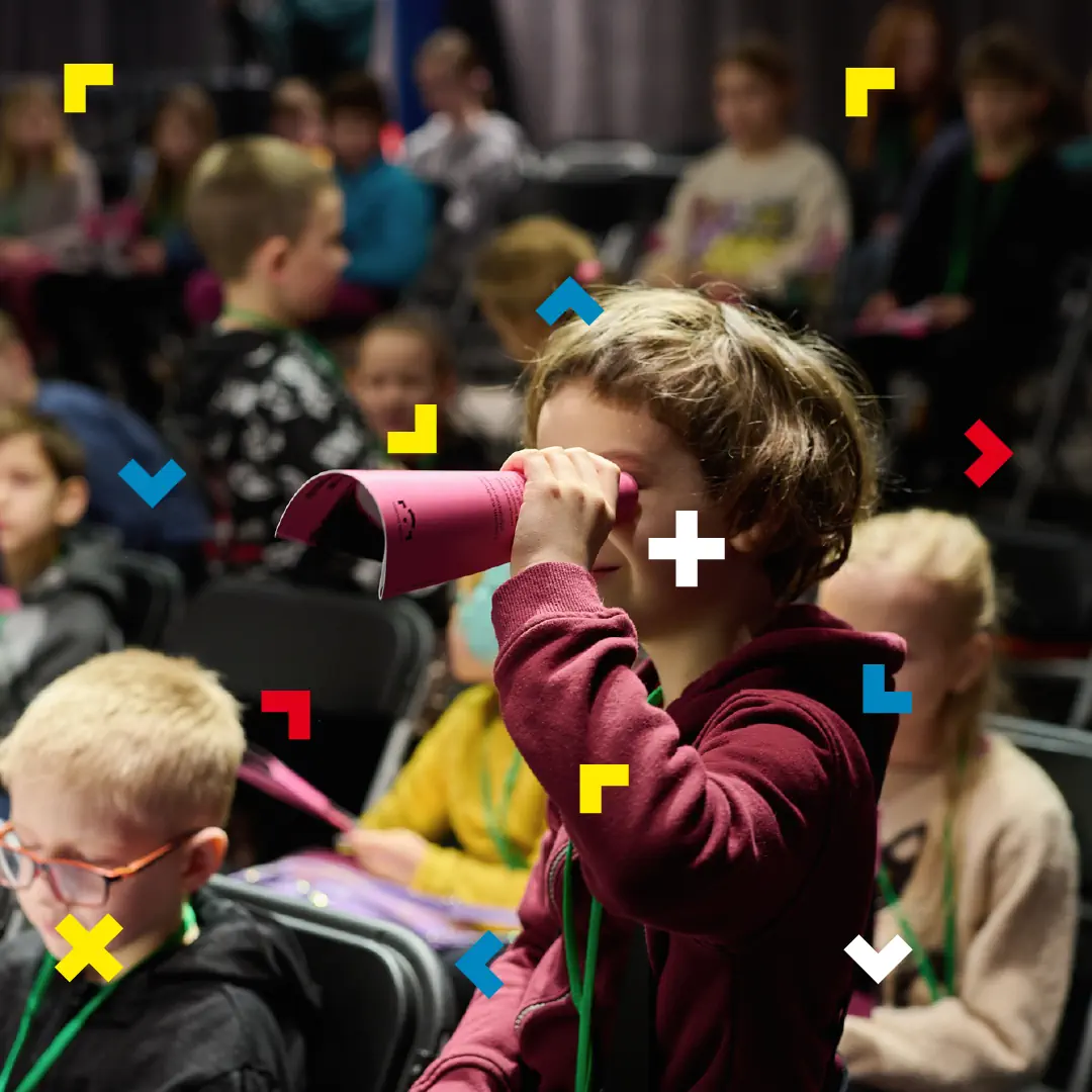 Dzieci oglądają film. Jeden chłopiec robi lunetę z książeczki.