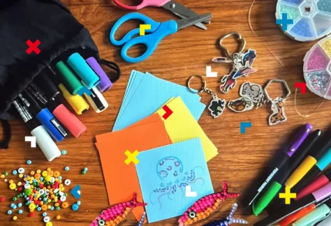 Na stole leżą mazaki, koraliki, nożyczki i kartki.