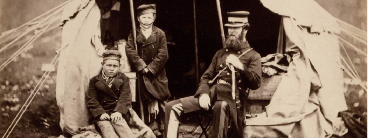 Na czarno-białym zdjęciu są dwaj chłopcy i mężczyzna. Stoją przed namiotem.