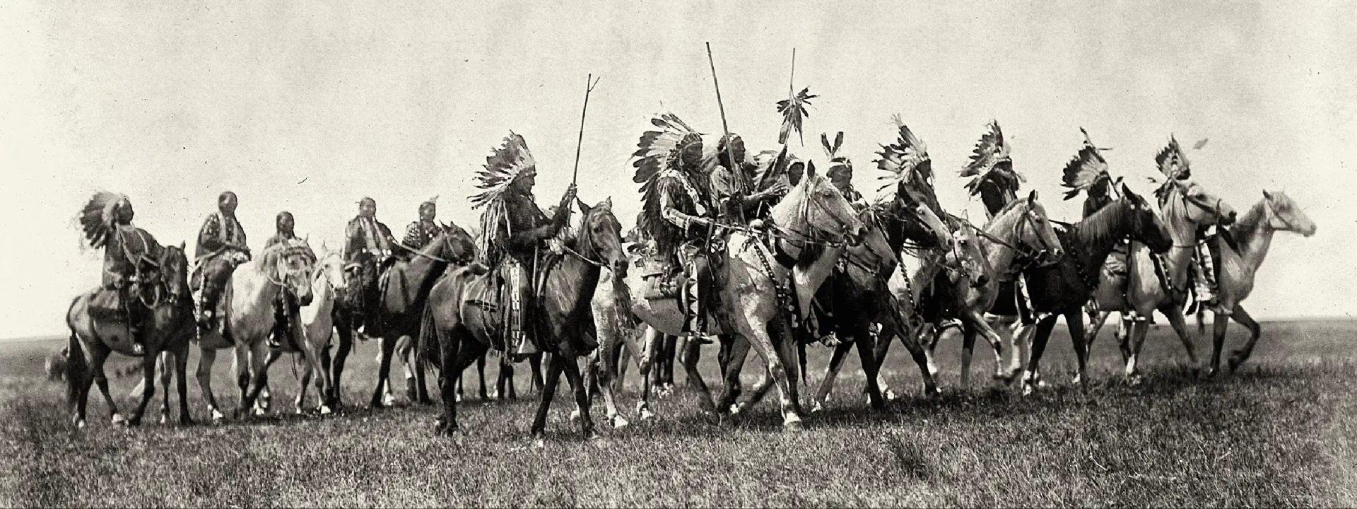 Czarno-białe zdjęcie Indian na koniach.