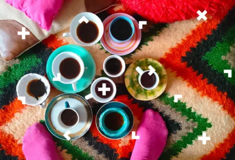 Stopy osoby, która stoi na dywanie. Ustawione są na nim też filiżanki z kawą i herbatą.