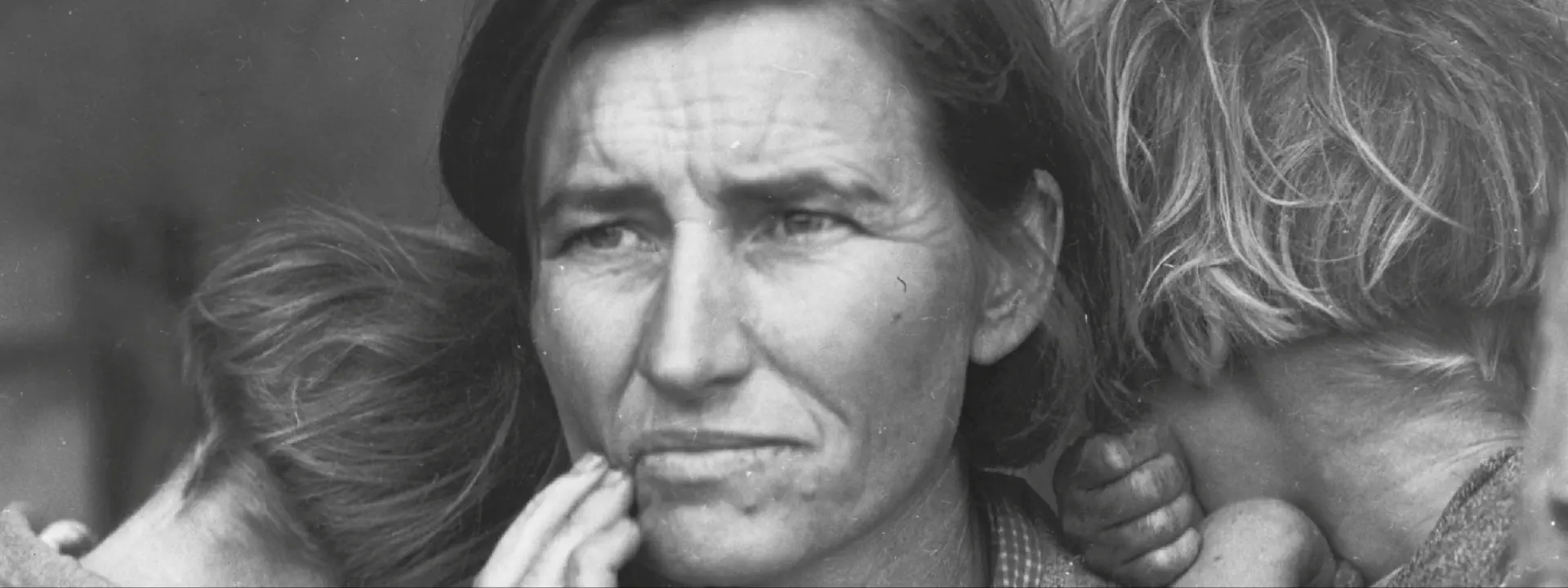 Czarno-białe zdjęcie kobiety z dwójką dzieci, które się do niej przytulają. Kobieta jest smutna.