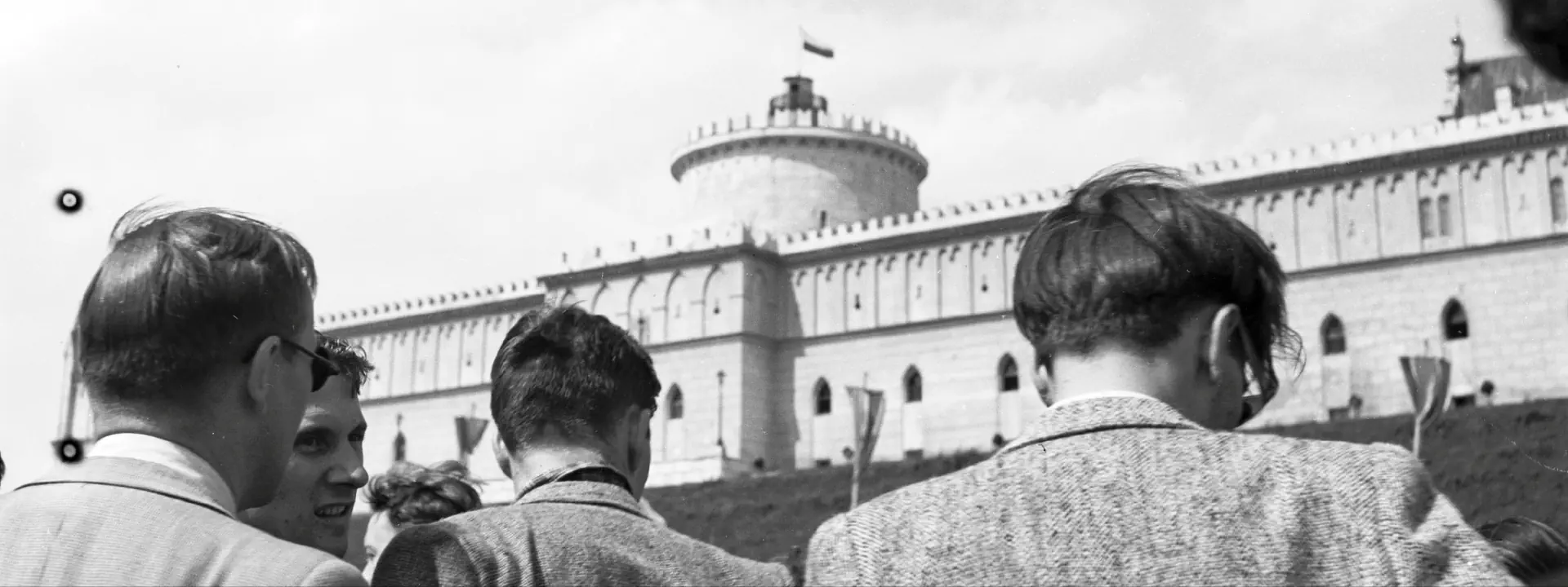 Czarno-białe zdjęcie zamku lubelskiego i zgromadzeni przy nim ludzie.