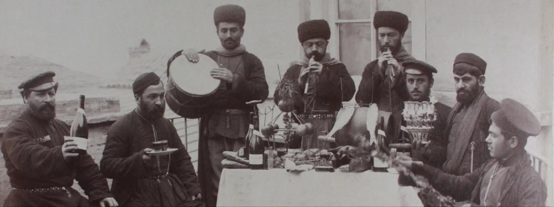 Czarno-białe zdjęcie grupy mężczyzn, którzy siedzą przy stole i grają na różnych instrumentach.