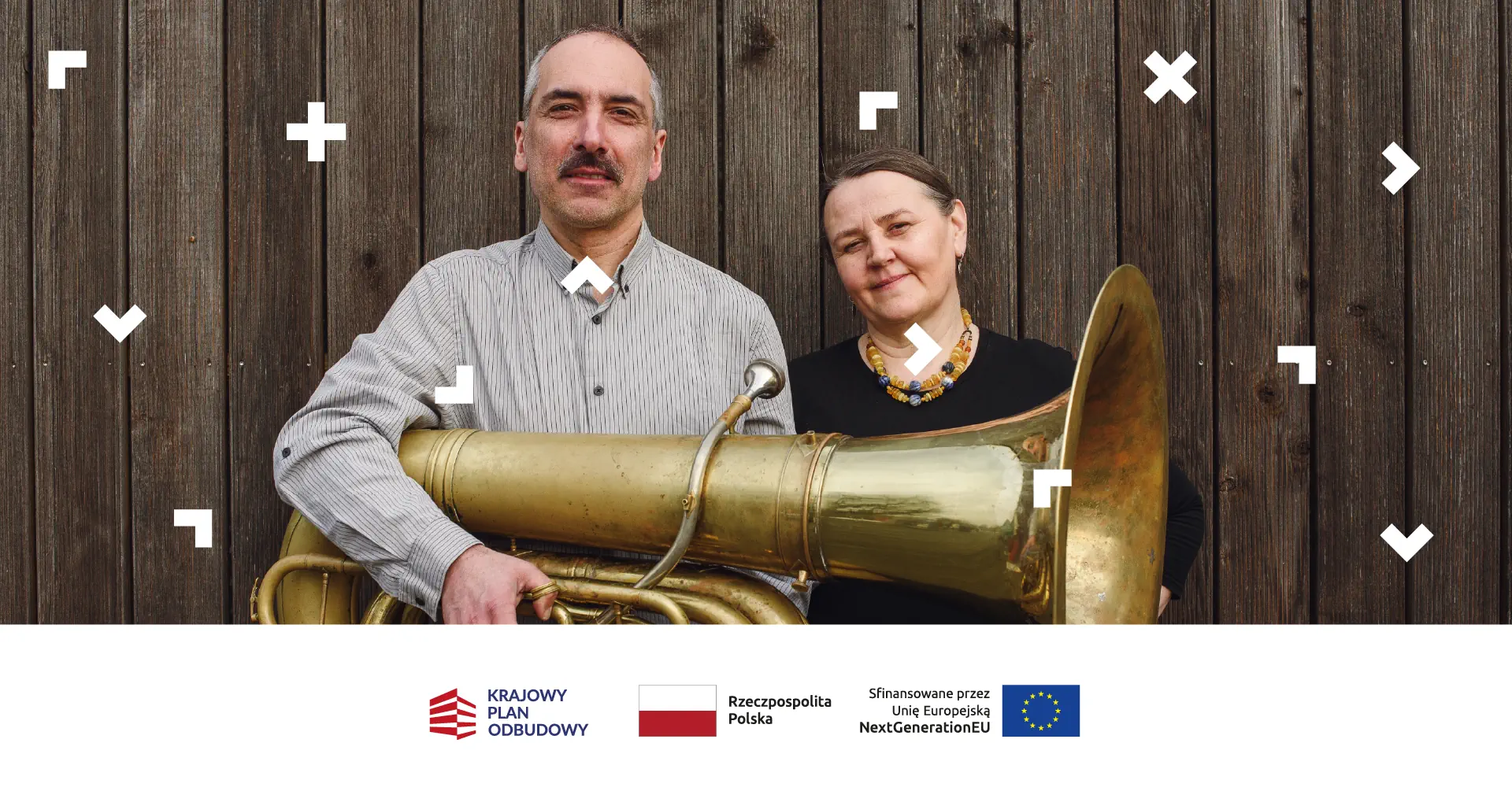 Kobieta i mężczyzna stoją pod drewnianym budynkiem. Trzymają w rękach saksofon.