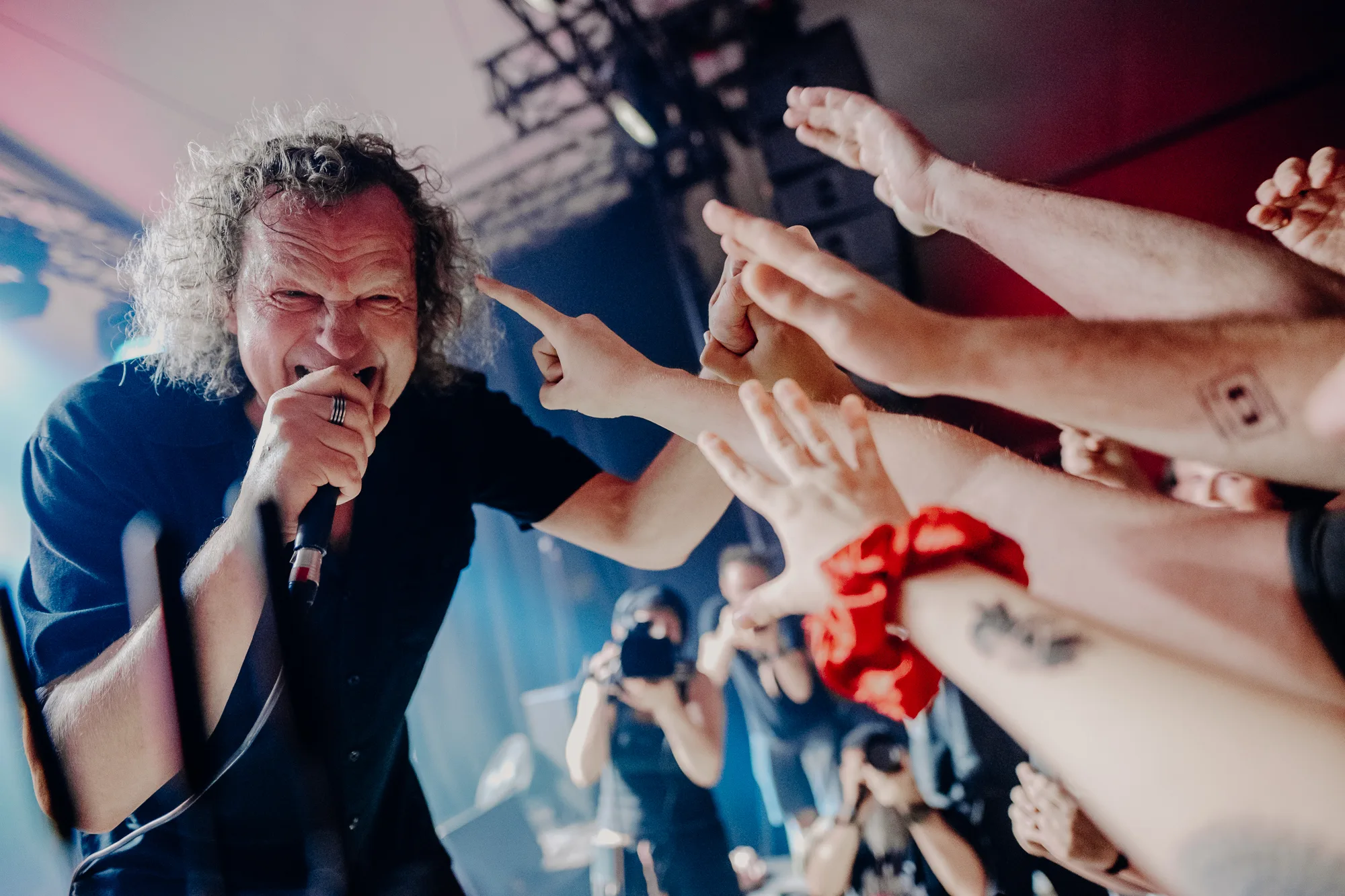 Artysta śpiewa pochylony w stronę publiczności. Ludzie machają rękami.