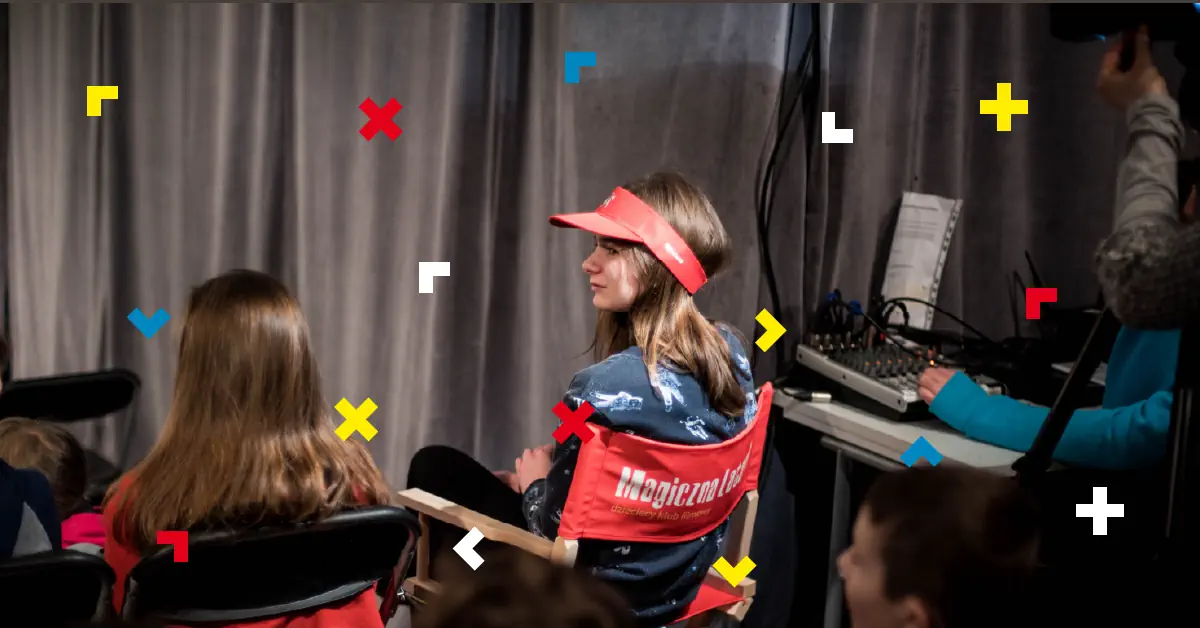 Dziewczyna siedzi na krześle z napisem Magiczna Latarnia. Ma też czapkę na głowie z tym samym napisem.