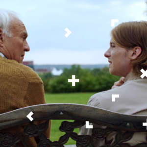 Kobieta siedzi na ławce ze starszym mężczyzną. Rozmawiają.