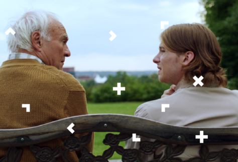 Kobieta siedzi na ławce ze starszym mężczyzną. Rozmawiają.