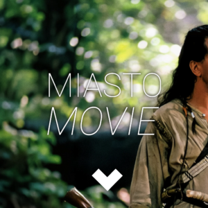 Mężczyzna z długimi włosami i dużą liczą broni stoi na skraju lasu. Na środku logo Miasta movie.