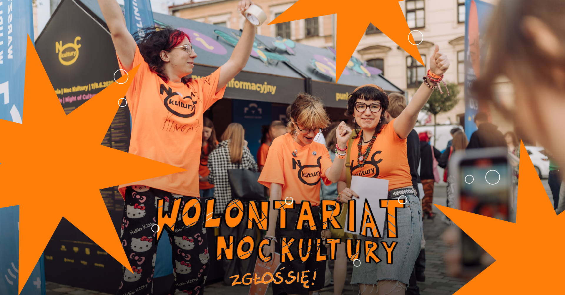 Grupa wolontariuszek podskakuje przed punktem informacyjnym.