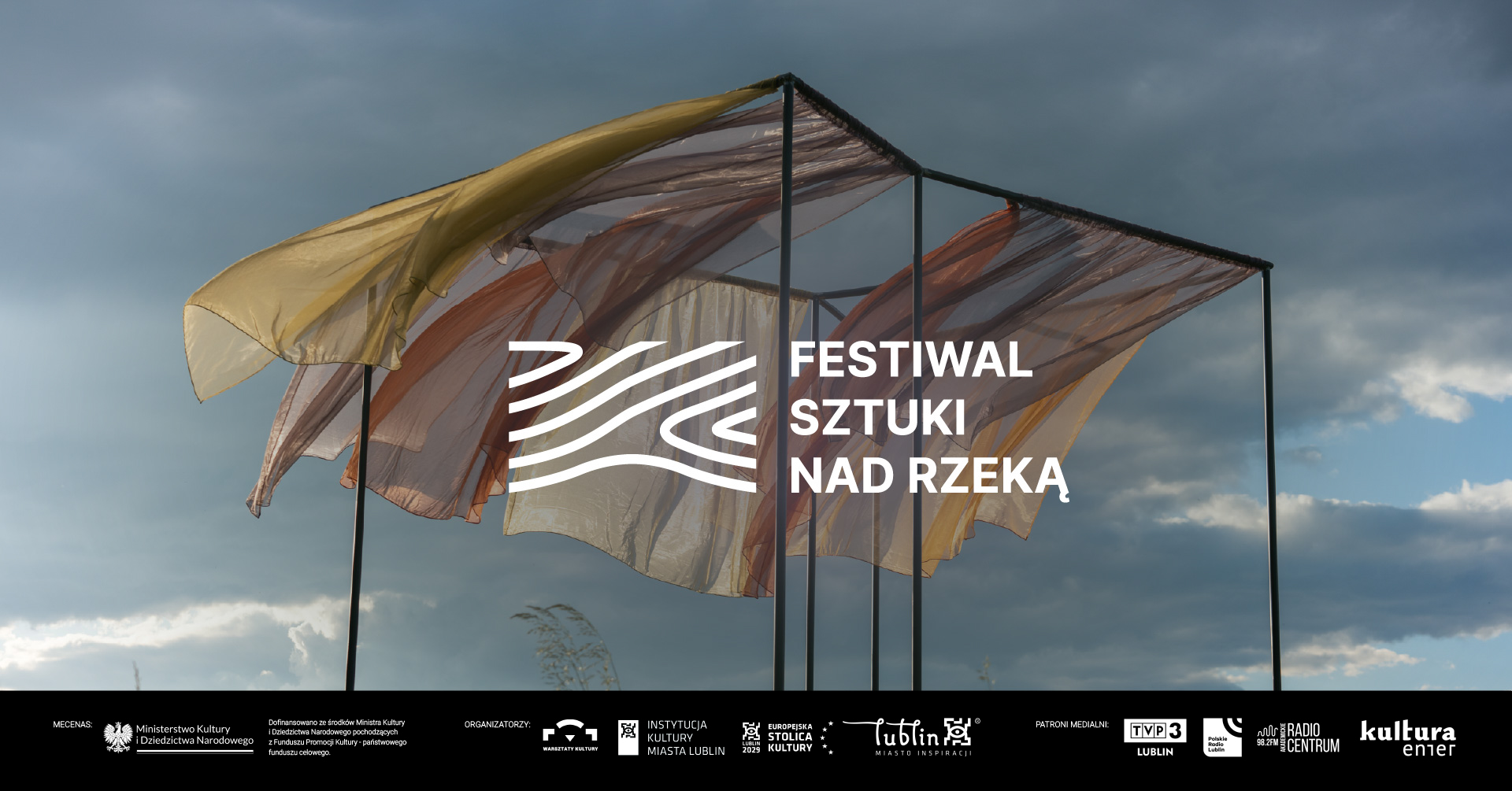 Zdjęcie szarf powiewających na wietrze. Napis: Festiwal Sztuki Nad Rzeką.