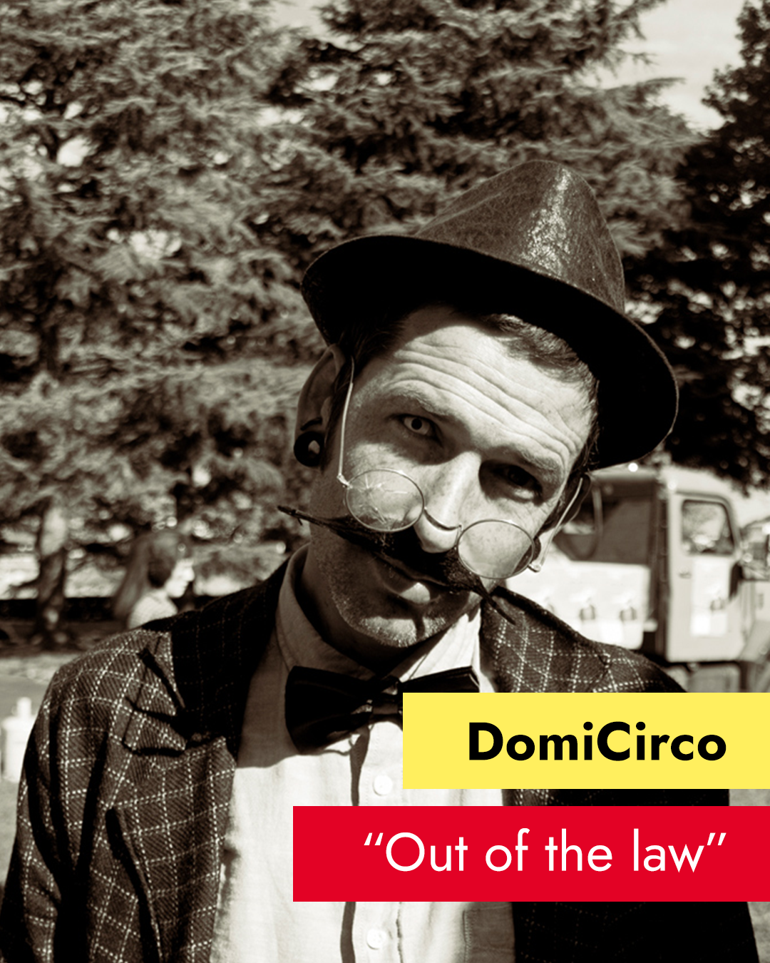 Artysta ma na głowie kapelusz, doczepiane wąsy i okulary. Napis: DomiCirco Out of the law.
