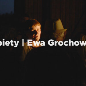 Kobieta rozmawia z mężczyznami. Napis: Kobiety | Ewa Grochowska.