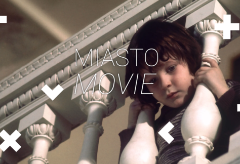 Kadr z filmu. Chłopiec wkłada głowę między barierkę na schodach. Napis Miasto Movie.